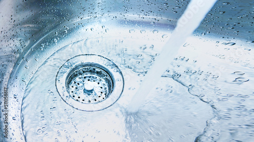 Banner with stream of clean water drink flows into the stainless steel sink. Sink plug hole close up, macro. Environment, water pollution and water shortage concept. Copy space for text