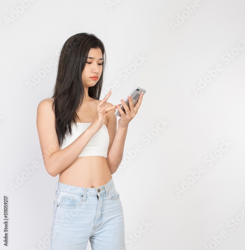 Portrait of a beautiful sexy young asian female lady in white color tube top fashion in happy mood video call and chat talking to her friend on a smartphone © asean studio