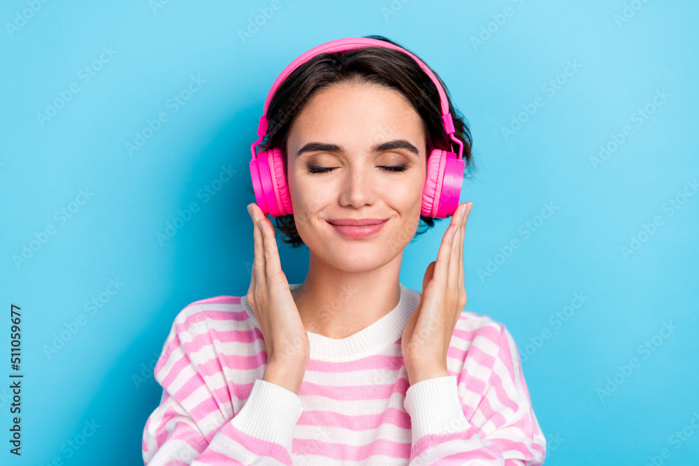 Close-up photo of adorable girl with closed eyes listening favorite music in pink headset isolated on blue color background Close-up photo of adorable girl with closed eyes listening favorite music in pink headset isolated on blue color background