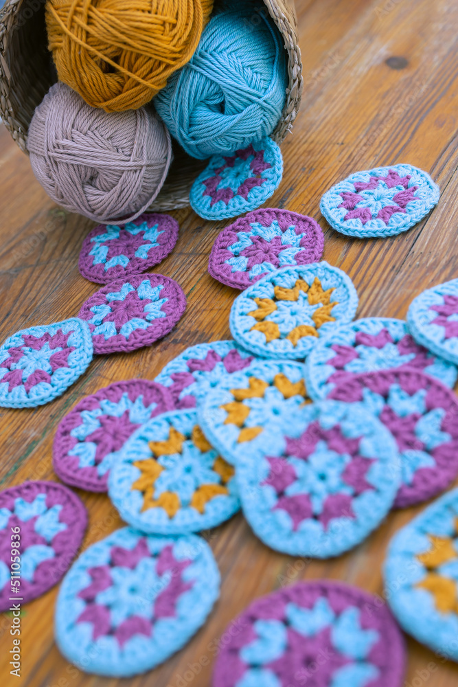 Multicolored crochet patterns overstrew on the wooden table and a small basket with cotton skeins in the corner. Multicolored crochet patterns overstrew on the wooden table and a small basket with cotton skeins in the corner.
