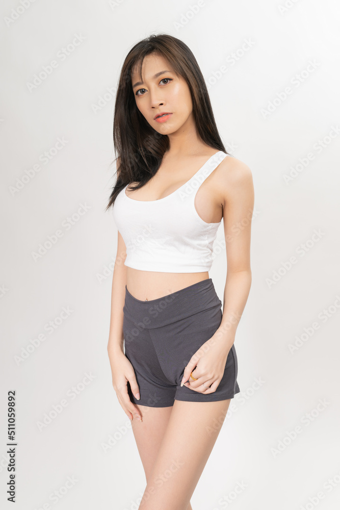 Naklejka premium Portrait of a young and sexy beautiful asian female lady model with nice body shape wearing white tops and grey pants for indoor exercise