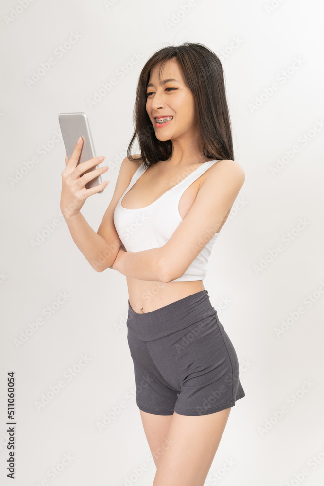 Portrait of a young and sexy beautiful asian female lady model with nice body shape wearing white tops and grey pants talking, selfie, video call and chit chat over a mobile phone Portrait of a young and sexy beautiful asian female lady model with nice body shape wearing white tops and grey pants talking, selfie, video call and chit chat over a mobile phone