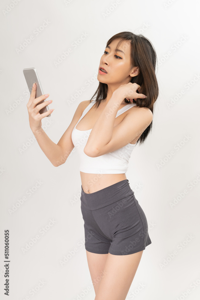 Portrait of a young and sexy beautiful asian female lady model with nice body shape wearing white tops and grey pants talking, selfie, video call and chit chat over a mobile phone