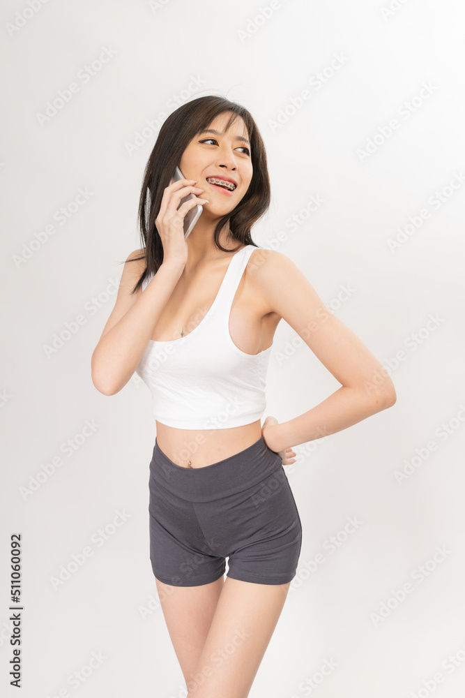 Portrait of a young and sexy beautiful asian female lady model with nice body shape wearing white tops and grey pants talking, selfie, video call and chit chat over a mobile phone Portrait of a young and sexy beautiful asian female lady model with nice body shape wearing white tops and grey pants talking, selfie, video call and chit chat over a mobile phone