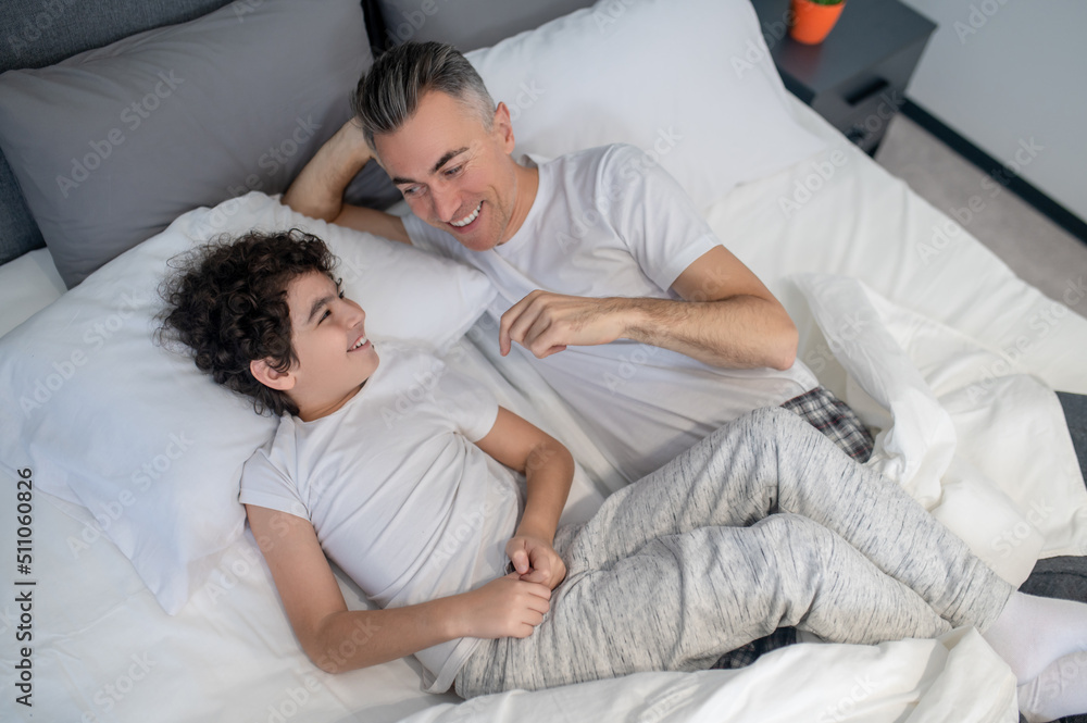 Father and son talking in bed in the morning and looking cheerful Father and son talking in bed in the morning and looking cheerful