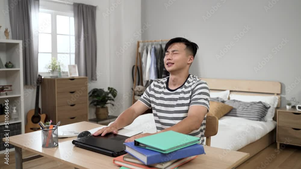 portrait of a tired asian college boy closing laptop with a sigh of relief after getting homework done while learning from home in his bedroom during lockdown portrait of a tired asian college boy closing laptop with a sigh of relief after getting homework done while learning from home in his bedroom during lockdown