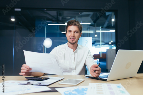 Portrait of a successful businessman at paper work, man smiling and looking at camera holding document and financial reports