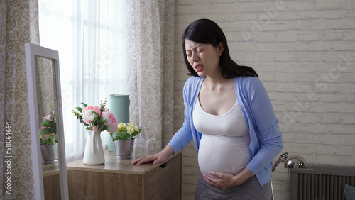 Photos pregnant woman walking to the home window is feeling a sudden contraction with her face contorted in a grimace of pain in the morning