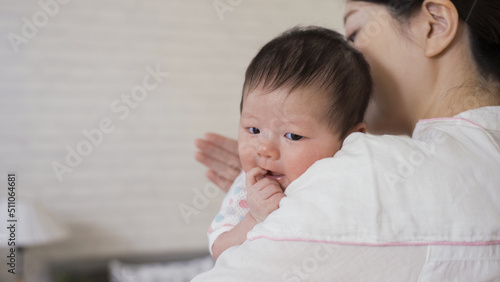 Konstfotografi selective focus cute newborn infant is looking at camera innocently as her mommy is helping her burp at blurred background bright nursery room