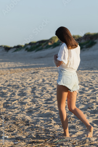 Young woman in denim shorts walking on beach.