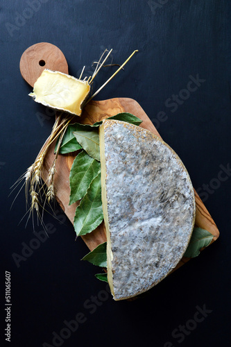 Saint Nectaire cheese with bay leaf on a cutting board. It is an Auvergne cheese and a mountain cheese made with cow’s milk.