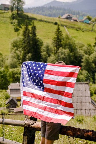 A young woman stands on a mountain and holds the US flag in her hands. American Independence Day celebration.