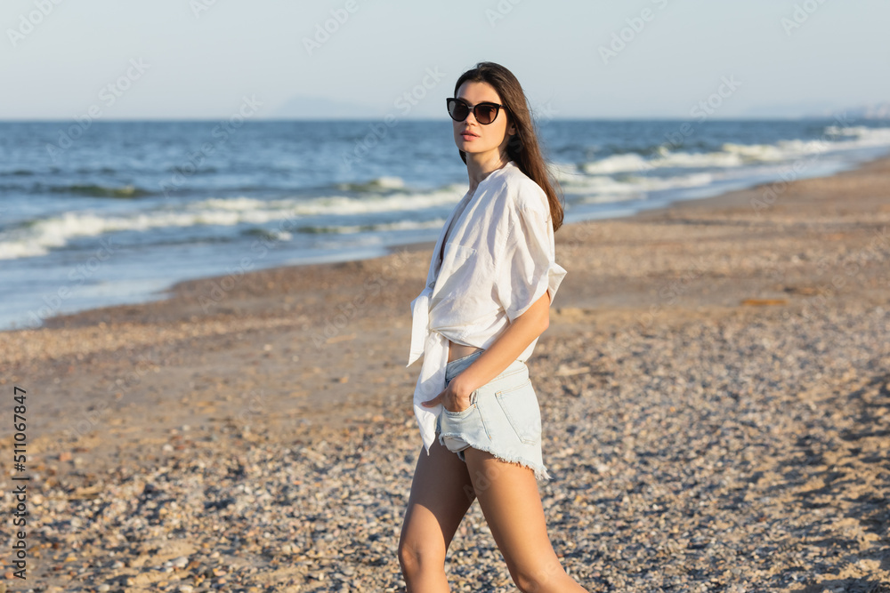 Woman in sunglasses and shirt standing on beach.
