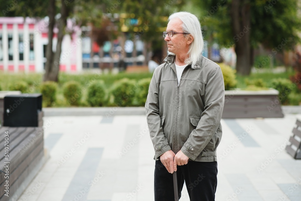 Elderly man walks with a cane in a city spring park. Elderly man walks with a cane in a city spring park.