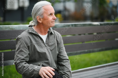 Old gray-haired man rest on the bench in summer park