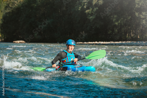 Male recreational athlete paddling carefully over the risky  foamy  and splashy whitewater rapids in his blue kayak