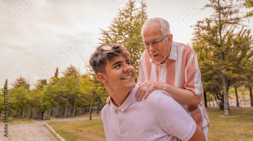 Foto Nieto joven, cogiendo a su abuelo al hombro, con expresión sonriente, pasándoselo bien en el parque
