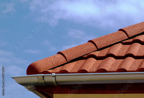 red brown sandy textured modern concrete roof tile closeup detail with half round ridge tiles. light gray silver shallow zink gutter. house construction concept. light blue sky background