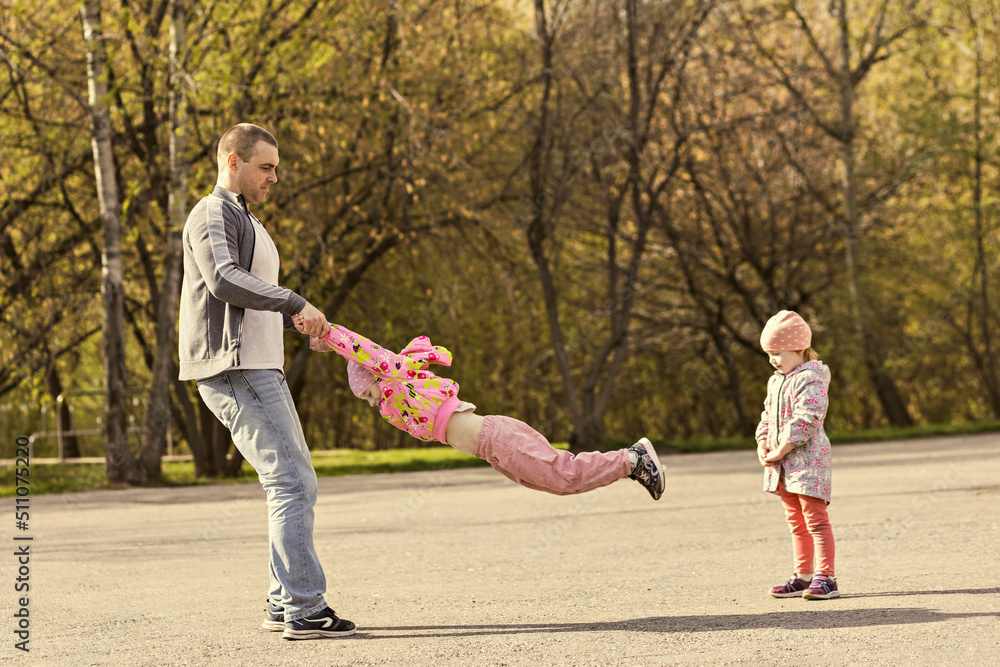 Dad plays with his daughters in the park. Twirling a girl around. Family Dad plays with his daughters in the park. Twirling a girl around. Family