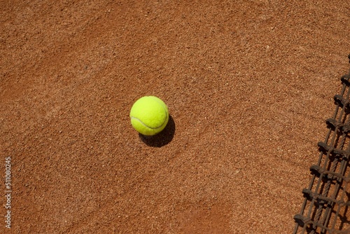 A tennis ball on a clay court and a tennis net. Copy space for text. Sports backgrounds.