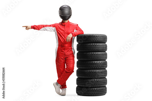 Full length portrait of a racer in a red suit and helmet leaning on a pile of tires and pointing to the side © Ljupco Smokovski