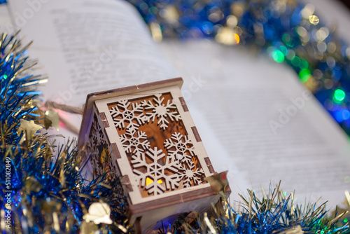 Closeup of the wooden flashlight with the carved snowflakes on the open book with the blue and golden tinsel. New year, Christmas background photo