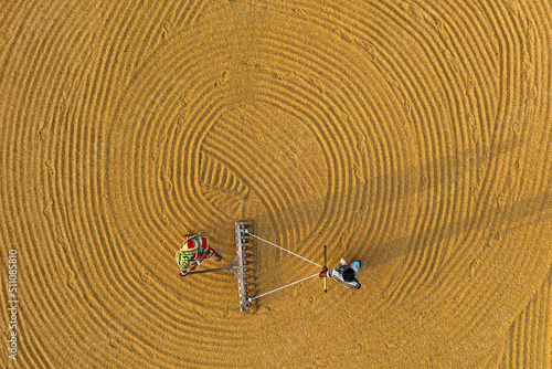 Workers working in small rice mill. Rice, paddy grain drying in sun. Flipping and weeping rice grains. Aerial view of rice mill. 