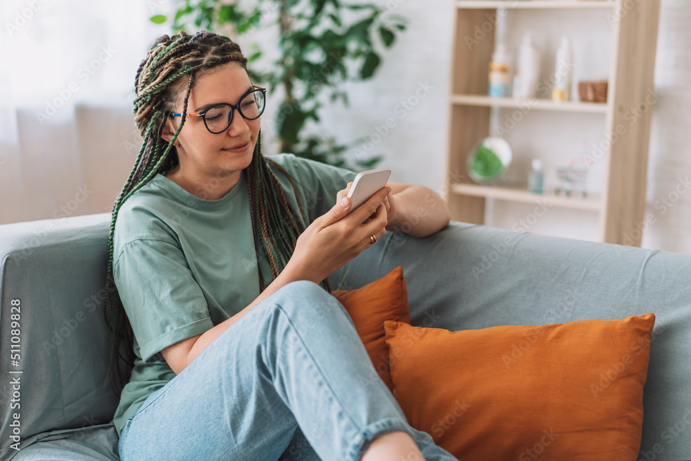 Obraz premium Girl with pigtails on her head holding smartphone while sitting on the couch.