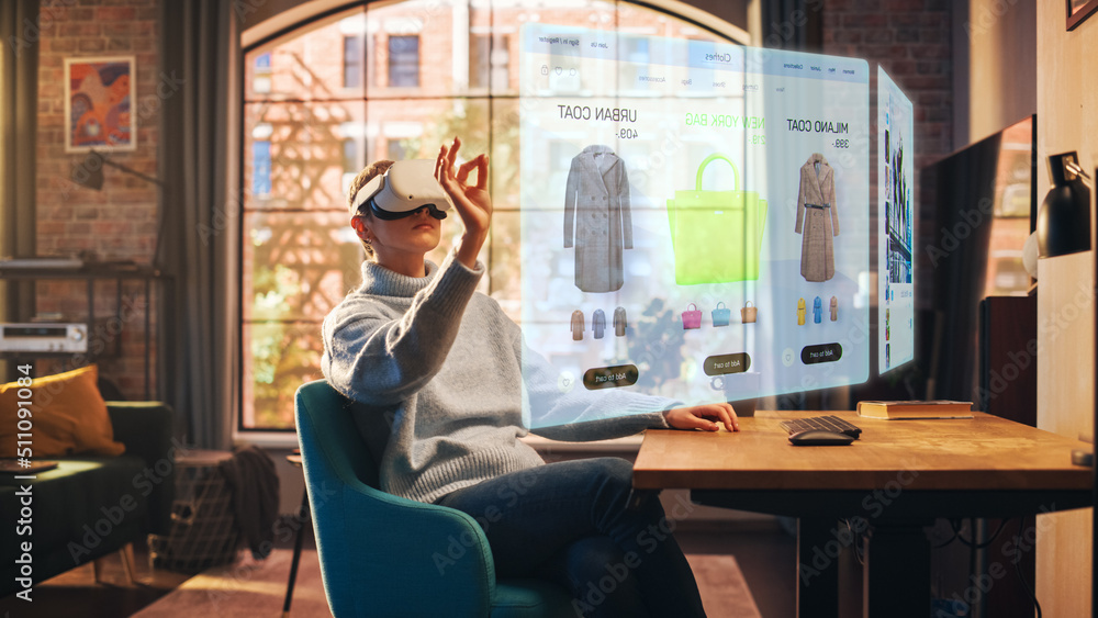 Young Beatiful Women is Using Virtual Reality Headset for Doing an Online Shopping In Stylish Loft Apartment. Casualy Dressed Female is Using Innovative Softwear to Purchase Cloth. 3D Website Concept. - obrazy, fototapety, plakaty 