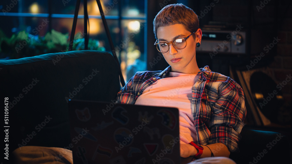 Young Beautiful Woman Resting on Couch, Using Laptop Computer in Stylish Loft Apartment in the Evening. Creative Female Smiling, Checking Social Media, Stretching. Urban City View from Big Window. - obrazy, fototapety, plakaty 