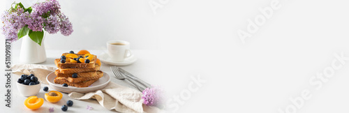 Trendy breakfast offer banner. Stack of delicious french toasts with berries, a cup of coffee and lilac flowers bouquet on white background. Copy space. Restaurant, backery web line. photo