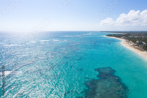 Bounty and pristine coastline with resorts, palm trees, caribbean sea and people having fun on beach. Dominican Republic. Aerial view