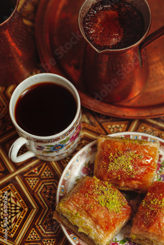 Still life with hot oriental coffee brewed in cezve. On the Arabic table is a small coffee cup and delicious honey baklava with pistachios on a saucer. View from above photo