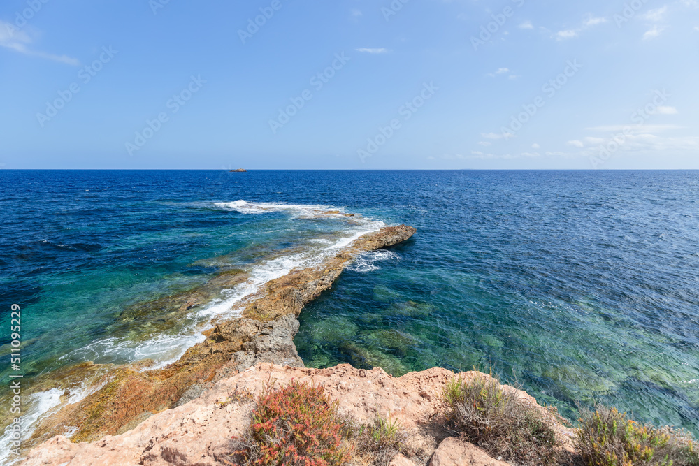 Section of the coastal rock descends into water in a thin long strip, leaving foaming sea waves on it, Ibiza, Balearic Islands, Spain