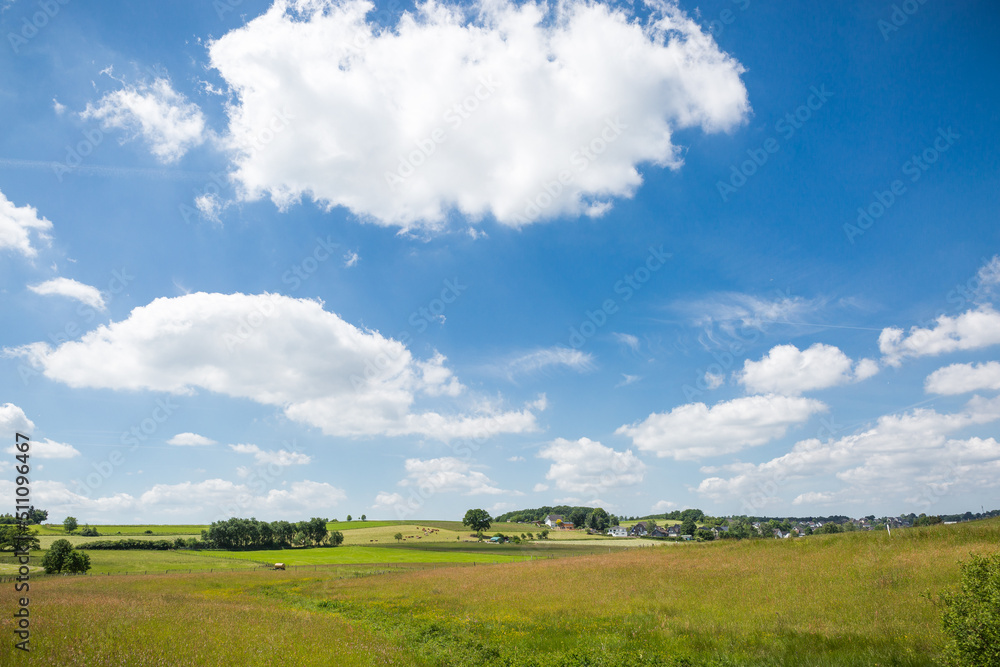Fototapeta premium Blauer Himmel und Wolken über Landschaft im Sommer