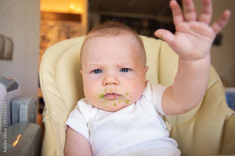 A baby soiled with vegetable puree sits in a children's chair A baby soiled with vegetable puree sits in a children's chair