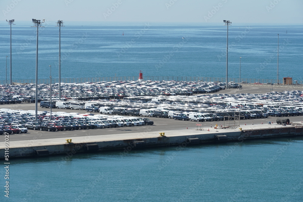 Valencia, Spain - 06 11 2022: New cars, lorries and busses are parking in port of Valencia, ready to be drive in auto shops for costumers. In background blue Mediterranean Sea.