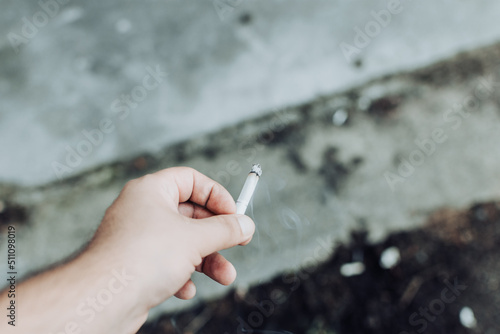 Man hand holding a cigarette an flicking the ash on the ground outside on a sidewalk with other cigarette butts photo