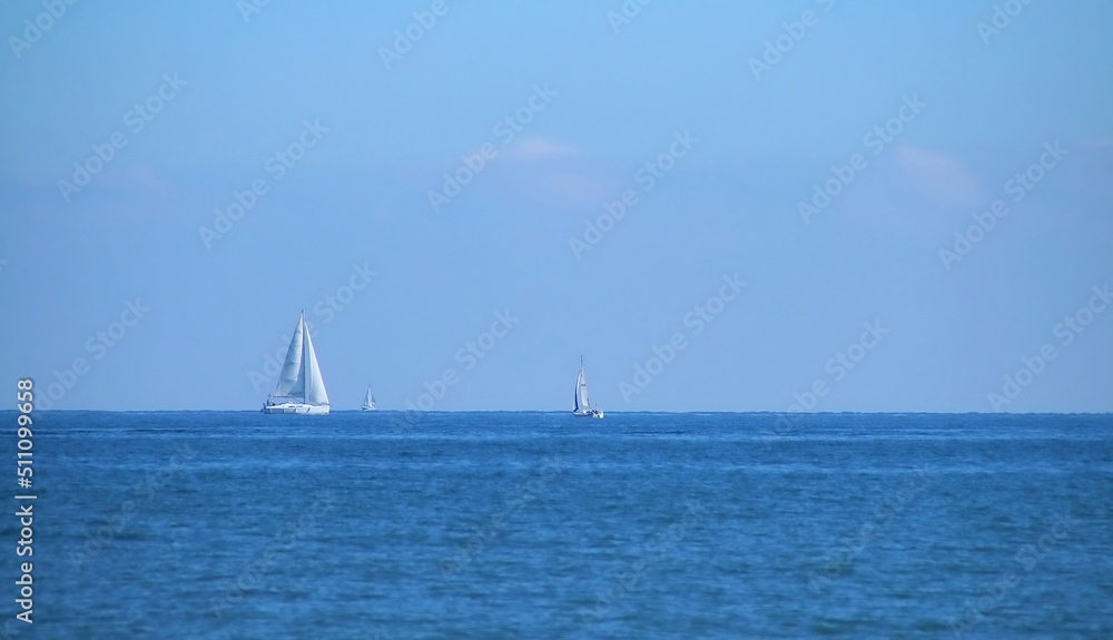 Barcos de vela navegando en el horizonte en la playa de la Malvarrosa en Valencia, España. El mar Mediterráneo con un azul intenso en un claro día de invierno.