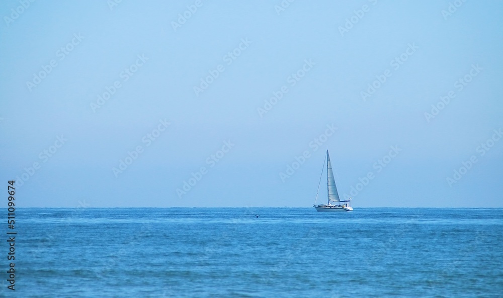 Barco de vela navegando en el horizonte en la playa de la Malvarrosa en Valencia, España. El mar Mediterráneo con un azul intenso en un día despejado de invierno.
