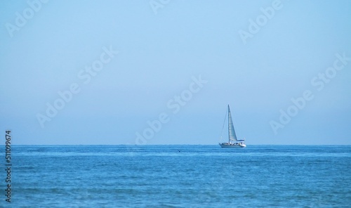 Barco de vela navegando en el horizonte en la playa de la Malvarrosa en Valencia, España. El mar Mediterráneo con un azul intenso en un día despejado de invierno.
