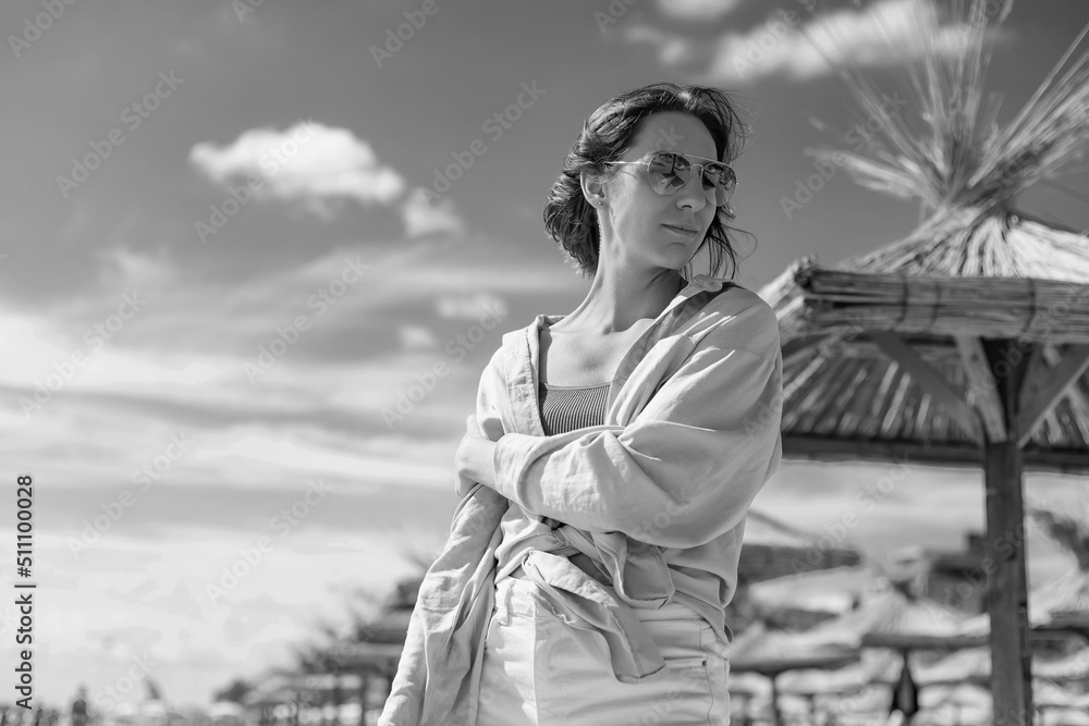 Fototapeta premium Smiling girl in sunglasses against a stormy sea. A bright sunny day. Straw sun loungers
