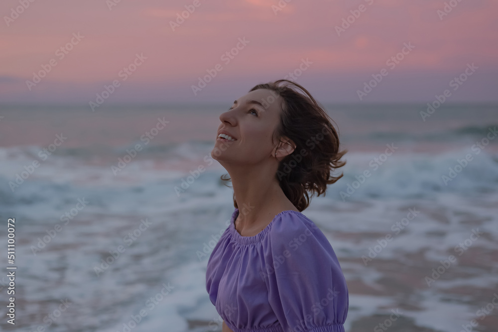 Smiling exquisite girl of European appearance in a short summer dress at dawn on the sea. Smiling exquisite girl of European appearance in a short summer dress at dawn on the sea.