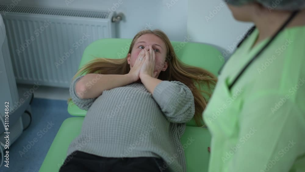 High angle view of frustrated shocked pregnant woman covering face with hands lying on examination couch in hospital. Unrecognizable obstetrician talking with patient telling bad news High angle view of frustrated shocked pregnant woman covering face with hands lying on examination couch in hospital. Unrecognizable obstetrician talking with patient telling bad news