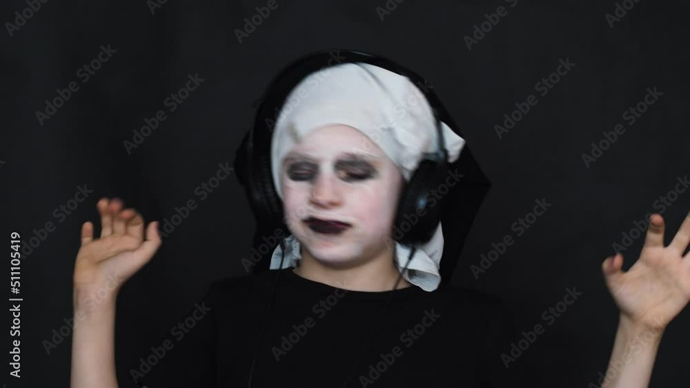  portrait of a cheerful caucasian boy 6-7 years old in a carnival black costume listens to music in headphones and dances, black studio background for shooting.Halloween celebration by children
