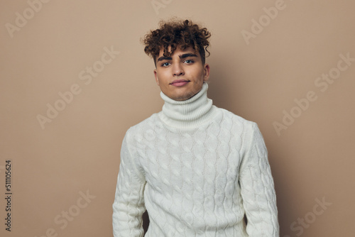 a close horizontal photo of a handsome, attractive man standing in a white knitted sweater on a beige background looking at the camera