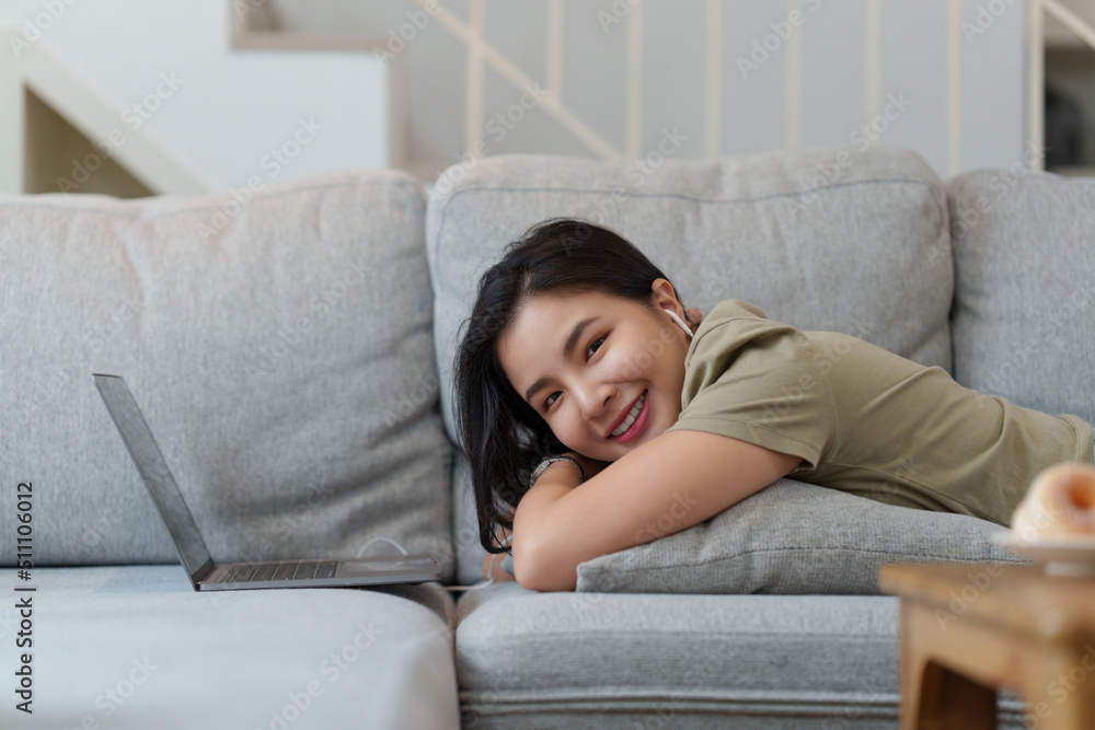Portrait of Happy Beautiful woman lay down on cozy couch and listen music by streaming on laptop. Portrait of Happy Beautiful woman lay down on cozy couch and listen music by streaming on laptop.