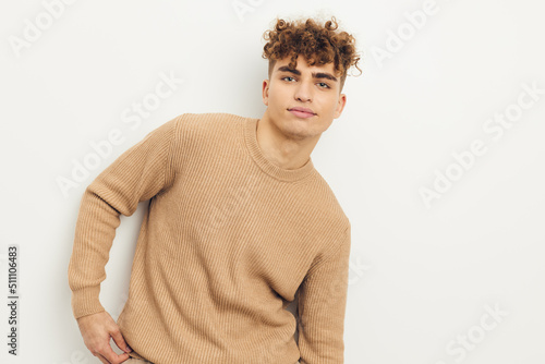 horizontal photo of a cute, pleasant man in a beige sweater looking at the camera while posing relaxed