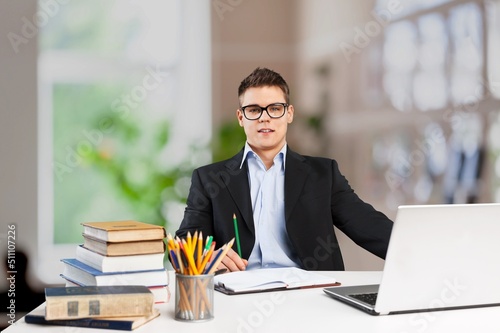 Smiling young businessman sitting at worktable at modern office,