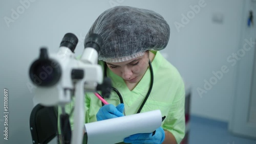 Concentrated expert obstetrician using gynecological colposcope writing with pen thinking. Portrait of expert Caucasian focused gynecologist doing examination in hospital indoors photo